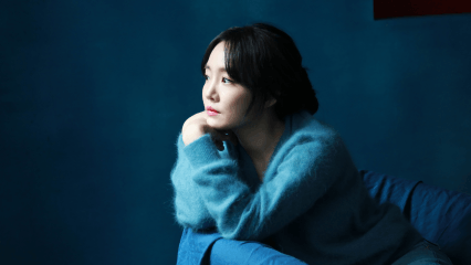 파란색 배경의 공간에서 파란색 옷을 입은 윤하가 파란색 소파 위에 왼쪽을 보고 앉아있다.